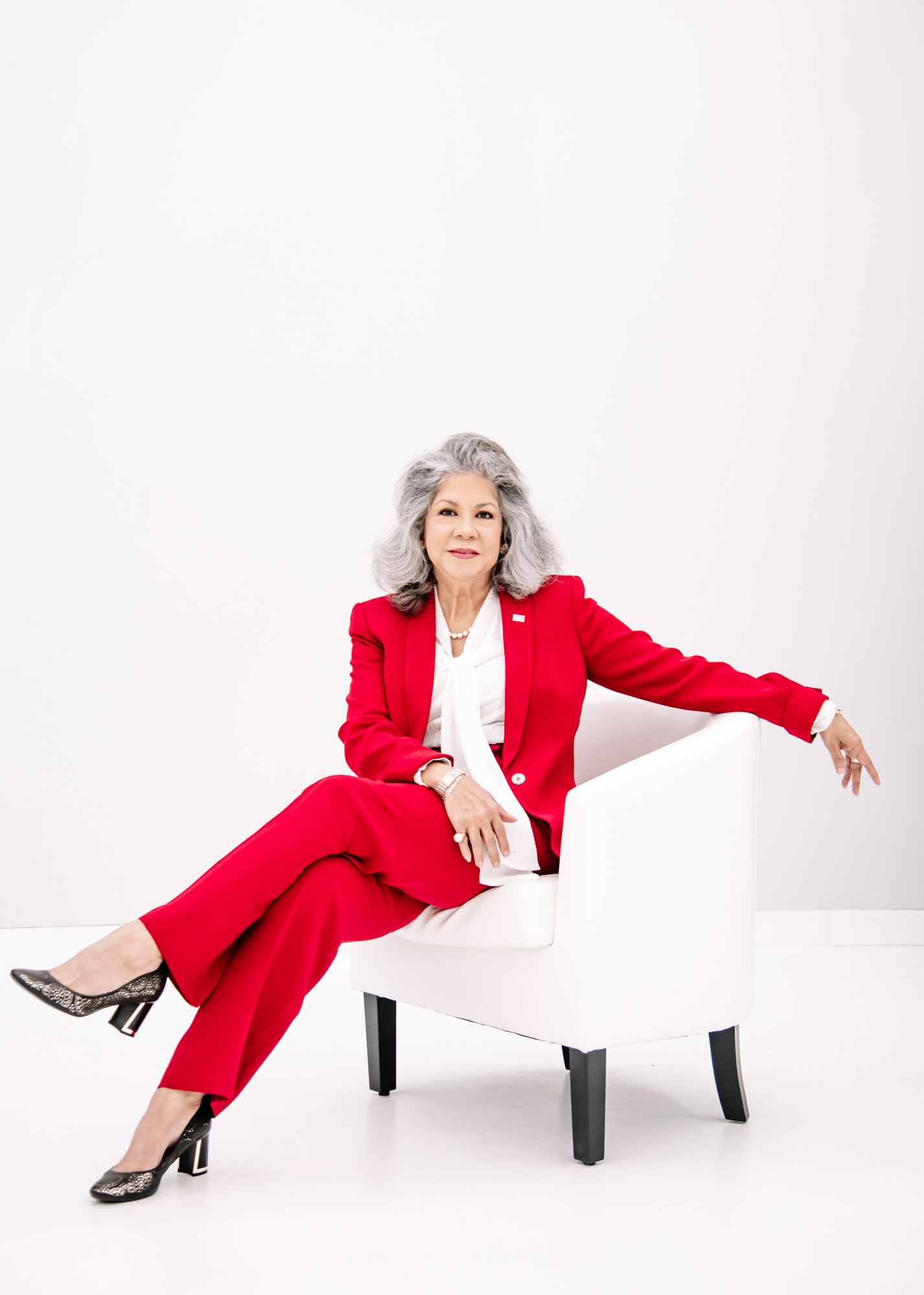 Lolita Smoak in a red pantsuit sitting stylishly on a white chair